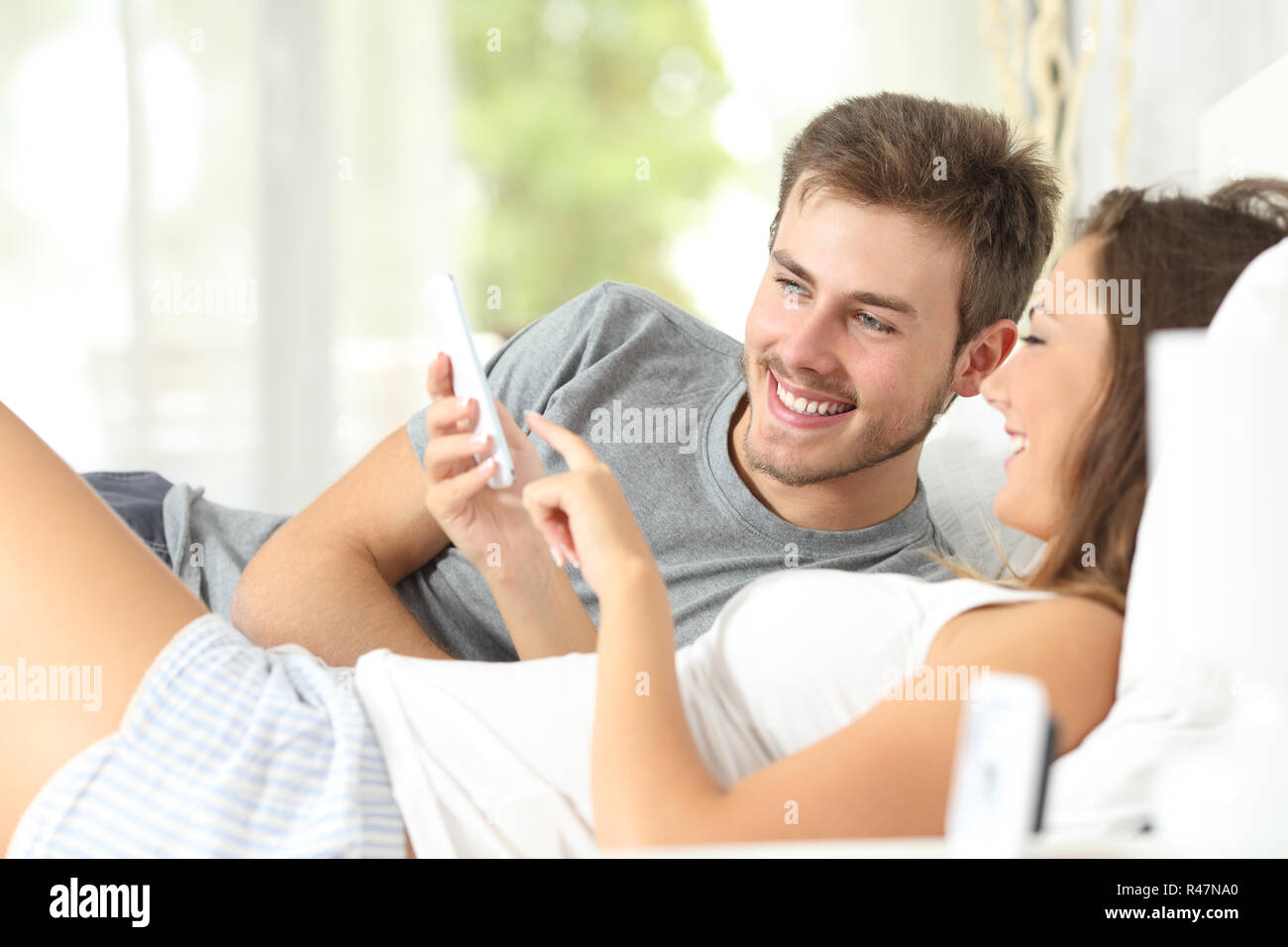 Paar teilen ein smart phone auf dem Bett Stockfoto