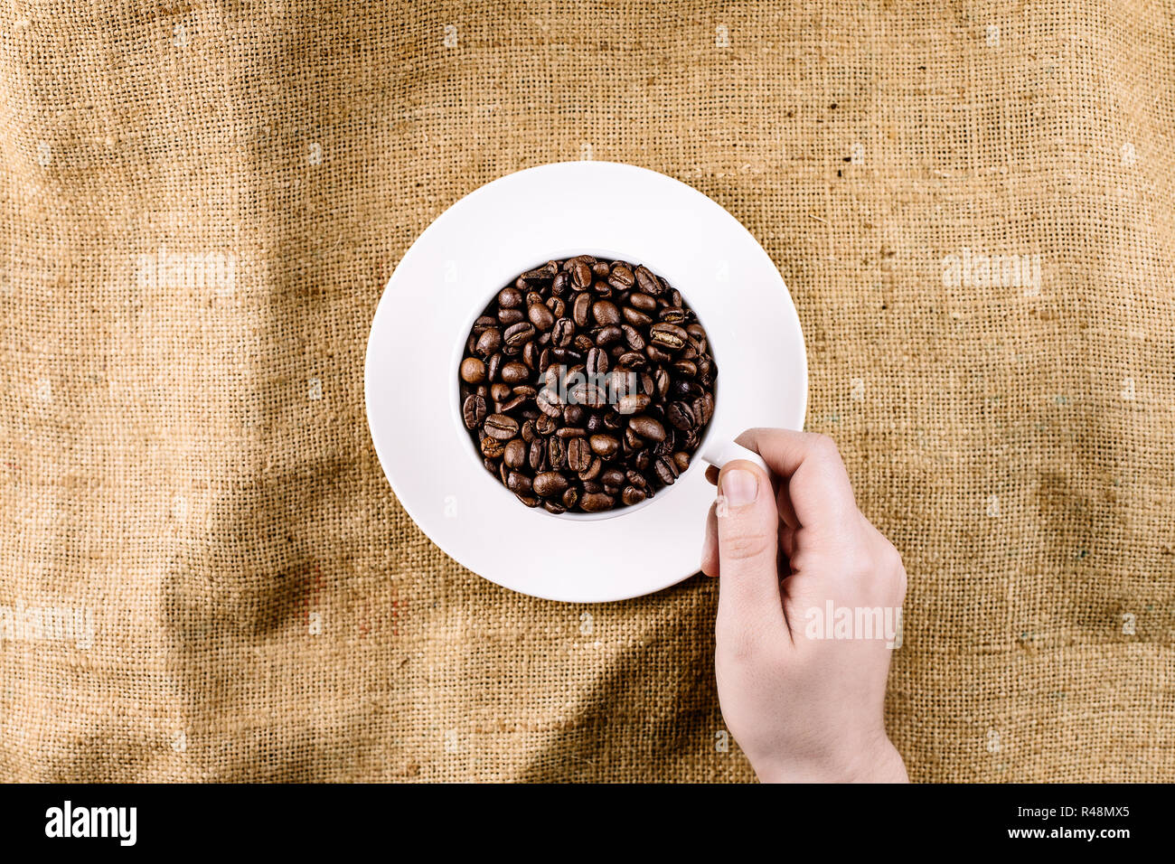 Eine Hand, die für eine Tasse mit Kaffeebohnen auf einem Braunen, strukturierten Hintergrund eingereicht Stockfoto