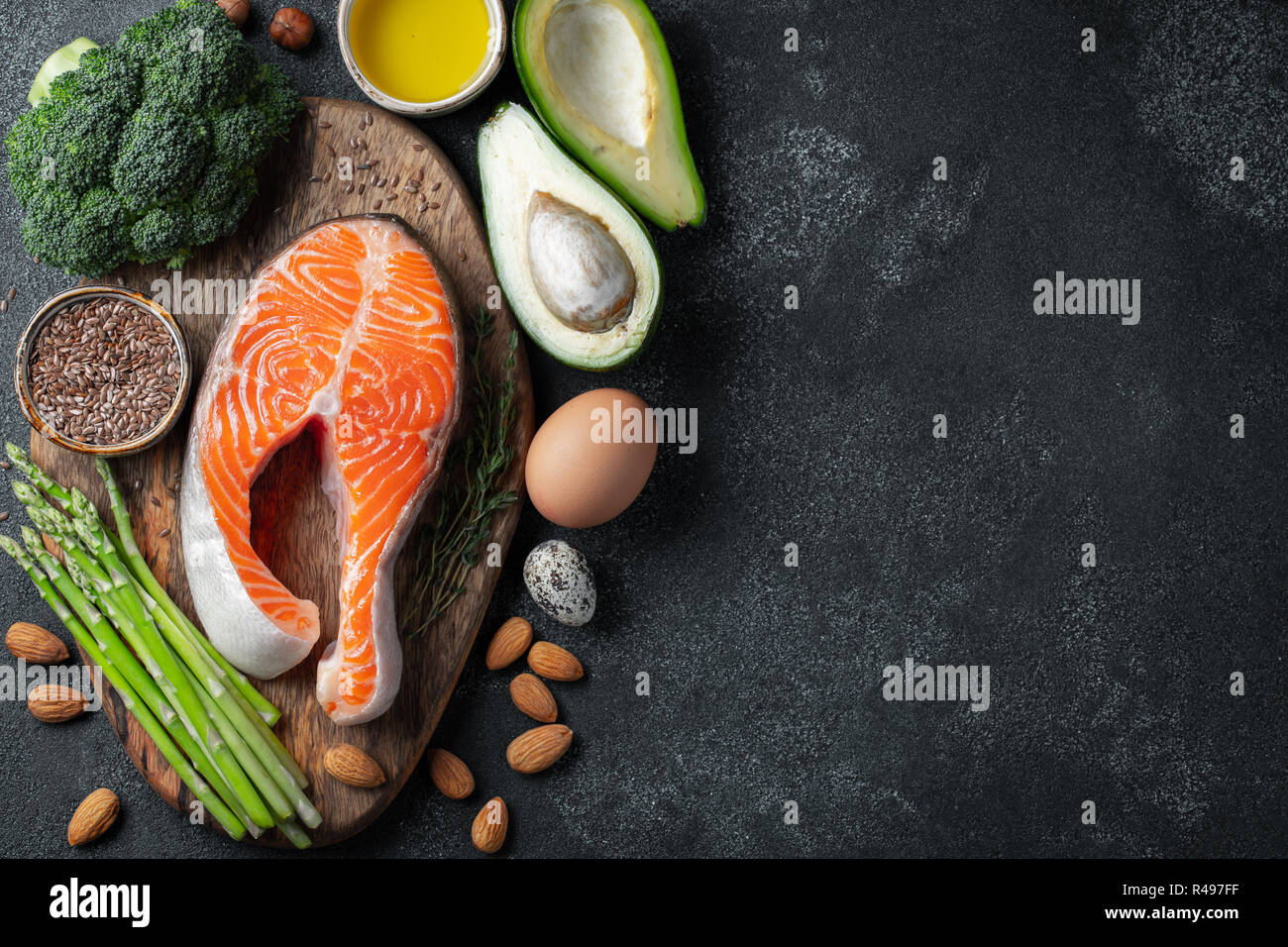 Eine Reihe von gesunden Lebensmitteln für keto Diät auf einem dunklen Hintergrund. Frische rohe Lachssteak mit Leinsamen, Brokkoli, Avocado, Huhn Eier, Nüsse und Spargel auf einem Holzbrett. Ansicht von oben mit der Kopie Raum Stockfoto