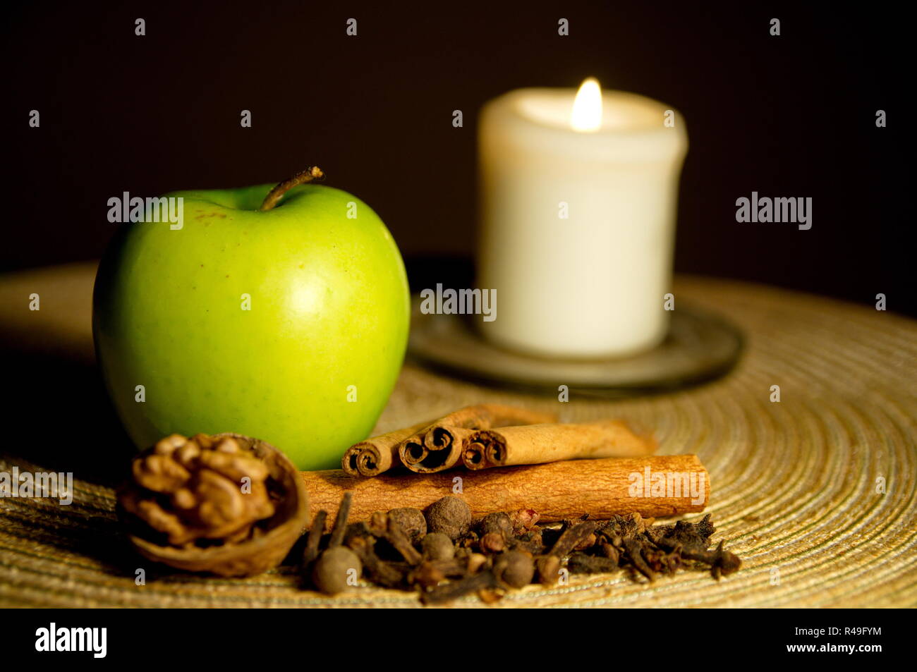 Grüner Apfel, Zimt, Walnuss und eine Kerze auf dem Tisch Stockfoto