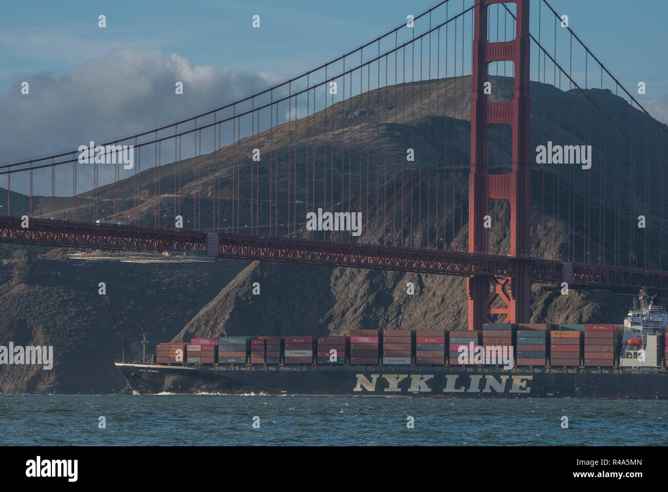 Ein Frachtschiff mit Lasten der Transportbehälter geht unter der Golden Gate Bridge in den späten Nachmittag. Stockfoto