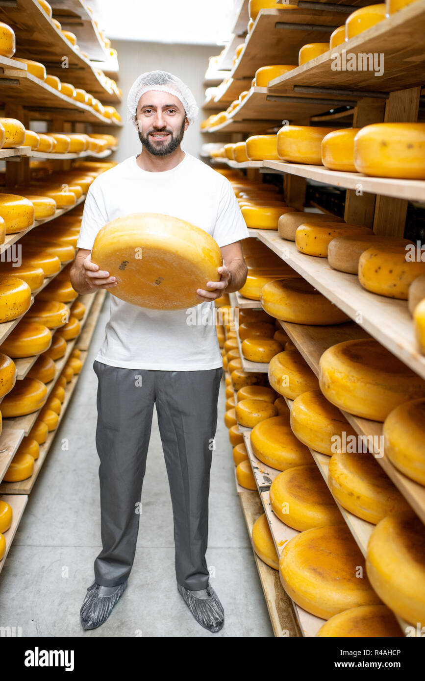 Porträt einer stattlichen Arbeitnehmer stehen mit Käse am Speicher voll der Käselaibe während des Alterungsprozesses Stockfoto