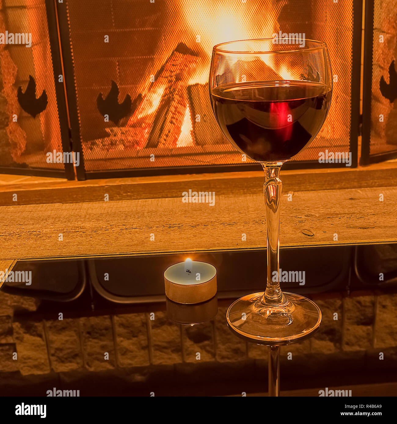Ruhige Szene vor dem gemütlichen Kamin mit einem Glas Rotwein und Kerzenschein, im Landhaus, im Winter Urlaub. Stockfoto
