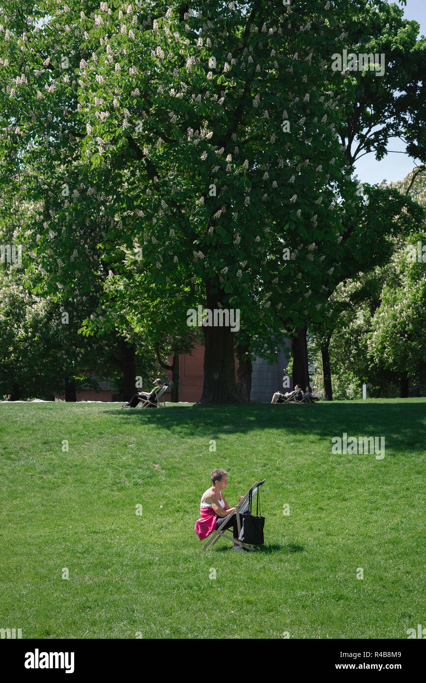 Konzept der sozialen Distanzierung, Ansicht einer Frau mittleren Alters, die allein sitzt und an einem Sommertag in einem Park zeichnet, Park Dabrowskiego, Posen, Polen. Stockfoto