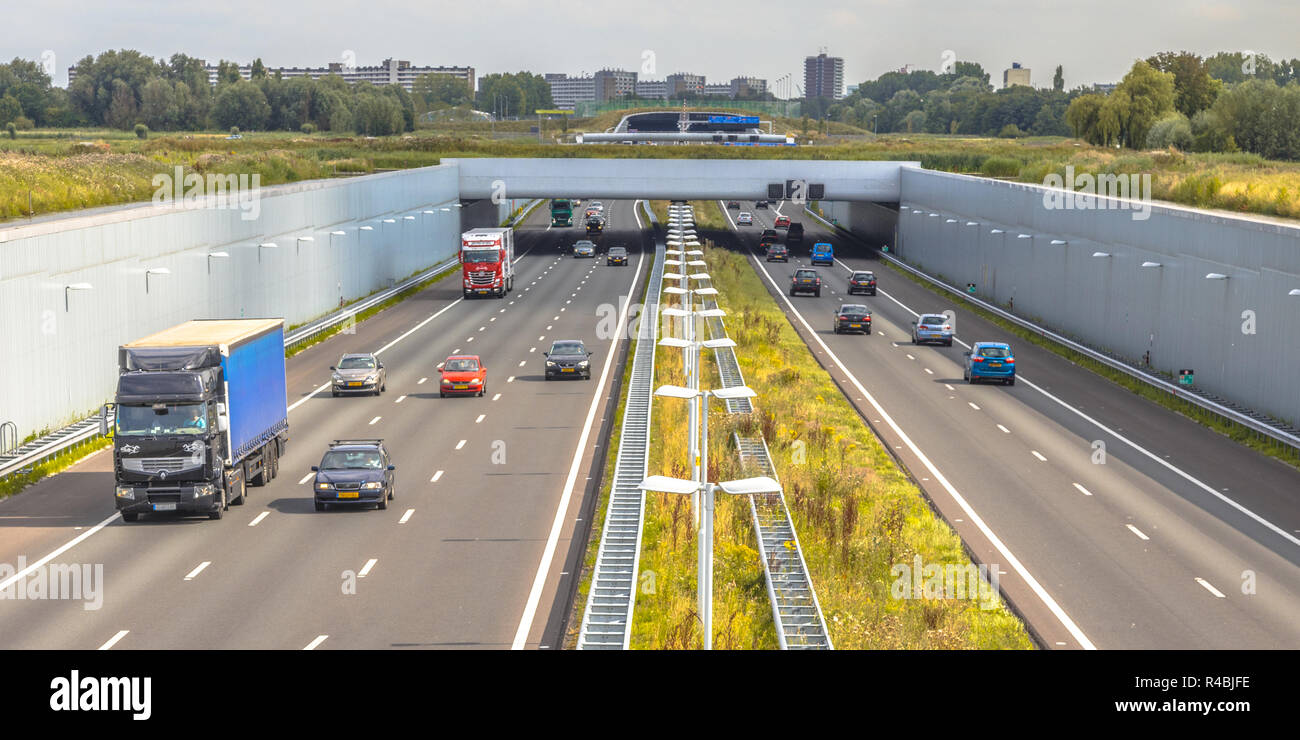 Morgen pendeln Verkehr auf der Autobahn a4 in der Nähe von Den Haag Gegend Randstad. Autobahn Kreuzung aquaduct Tunnel mit städtischen Gebiet von Rotterdam im Hintergrund, Neth Stockfoto