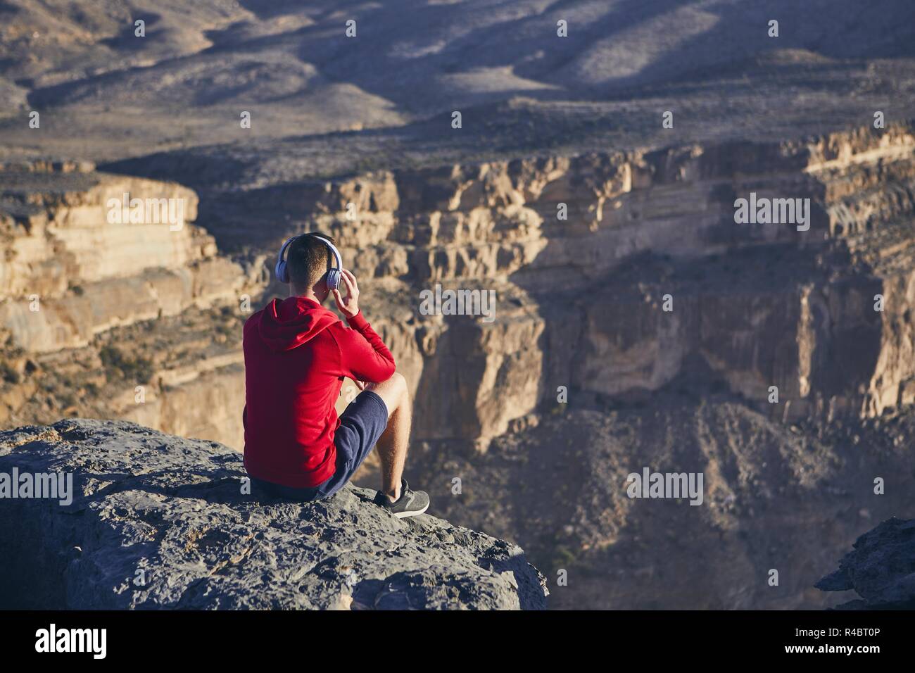 Entspannung in den Bergen. Junger Mann mit Kopfhörer sitzen auf den Rand der Klippe und hören Musik. Jebel Akhdar, Grand Canyon von Oman. Stockfoto