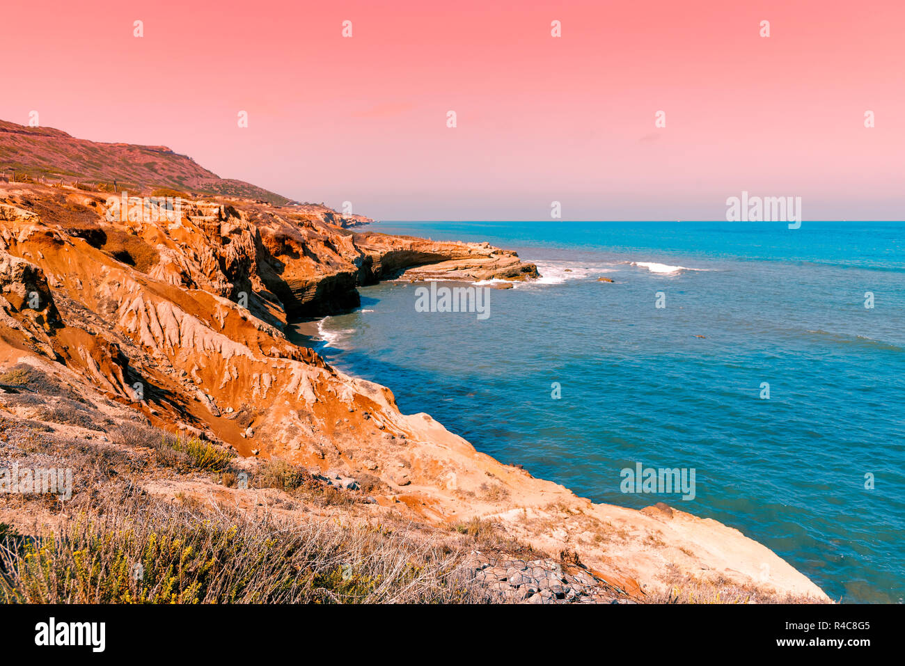 Sonnenuntergang auf felsigen Bucht mit türkisfarbenem Ozean darunter, und orange rosa Himmel oben. Stockfoto