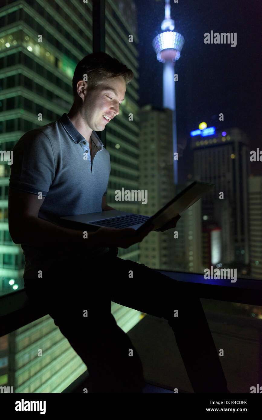 Junger stattlicher Mann mit Laptop gegen Glasfenster mit Blick o Stockfoto