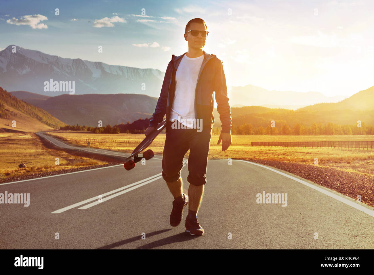 Glücklicher Mensch skater Spaziergänge mit Longboard durch Sonnenuntergang Mountain Road. Eislaufen oder longboarden Konzept Stockfoto