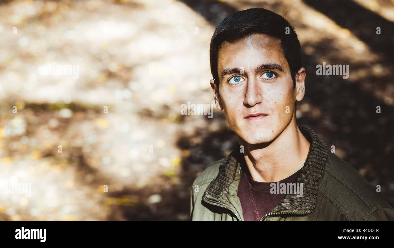 Attraktiven jungen Mann mit wunderschönen blauen Augen vorne suchen, mit dem Bokeh der Natur der Hintergrund Stockfoto