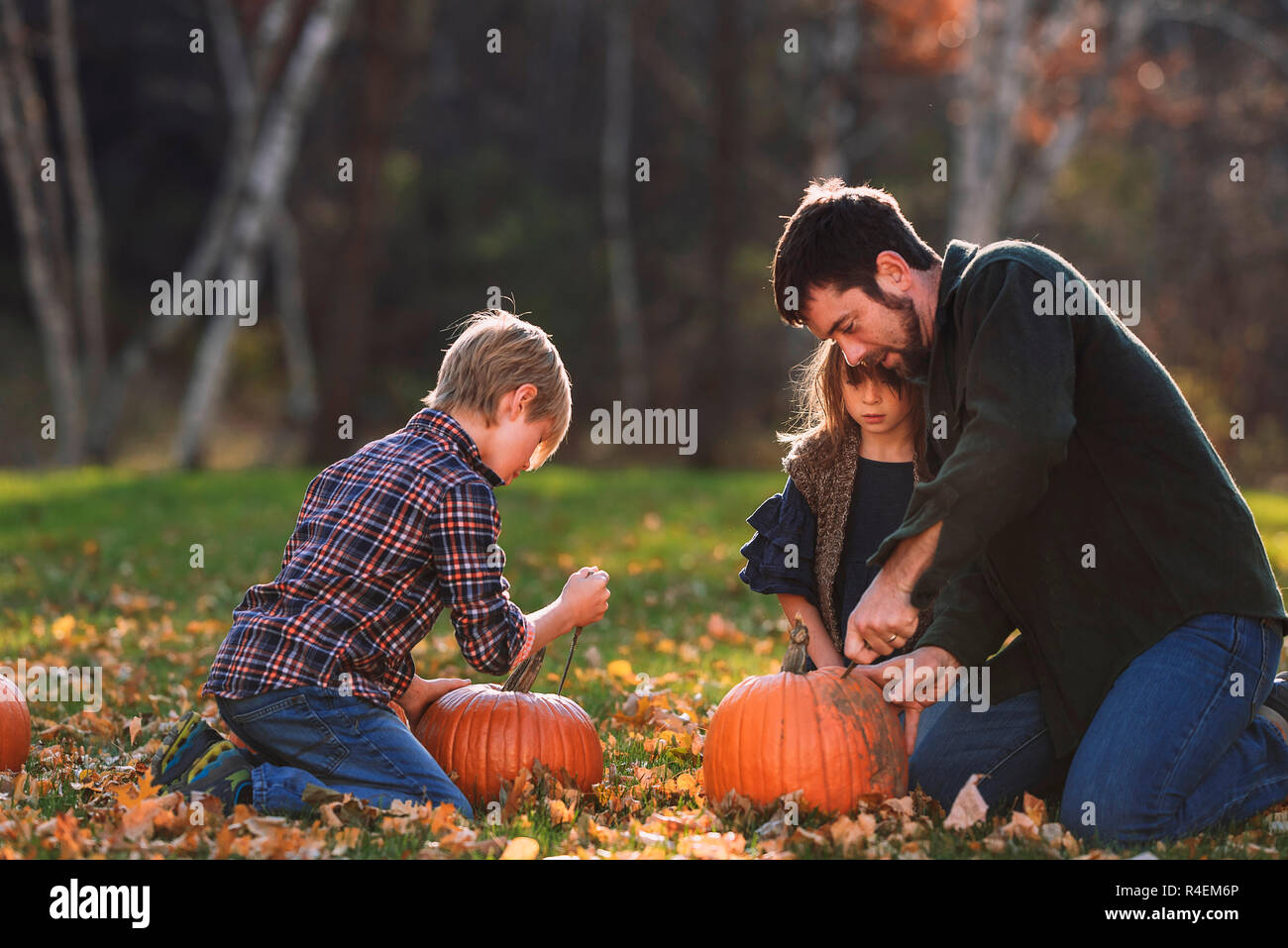 Vater und zwei Kinder sitzen im Garten schnitzen Halloween Kürbisse, United States Stockfoto