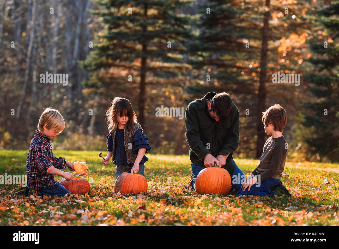 Vater und drei Kinder schnitzen Halloween Kürbisse im Garten, United States Stockfoto