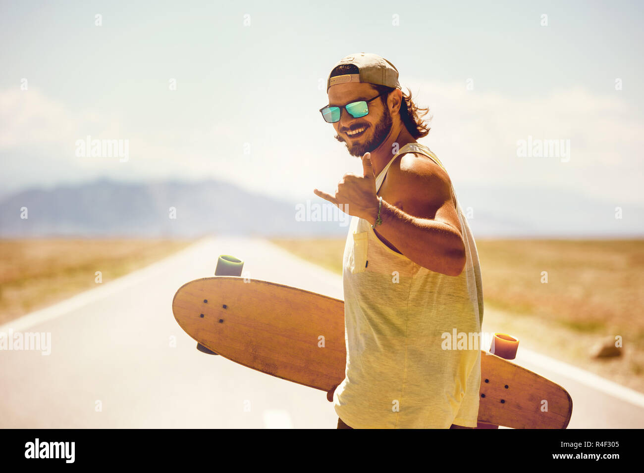 Happy athletischer Mann mit Skateboard oder Longboard durch geraden Straße Stockfoto