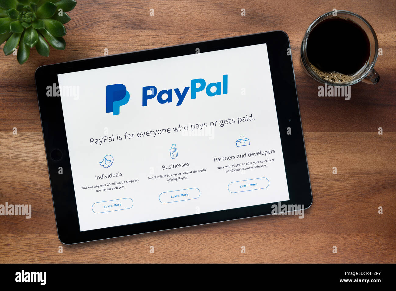 Die Website von PayPal ist auf einem iPad Tablet gesehen, auf einer hölzernen Tisch zusammen mit einem Espresso und einem Haus Anlage (nur redaktionelle Nutzung). Stockfoto
