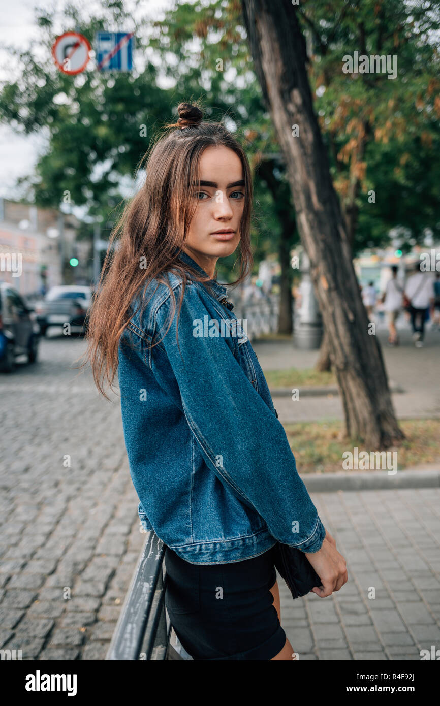 Schöne Mädchen in Blue Denim Jacke und Hosen auf der Straße der Stadt  lehnte sich auf Attika an Kamera suchen mit ruhigen Gesichtsausdruck  Stockfotografie - Alamy