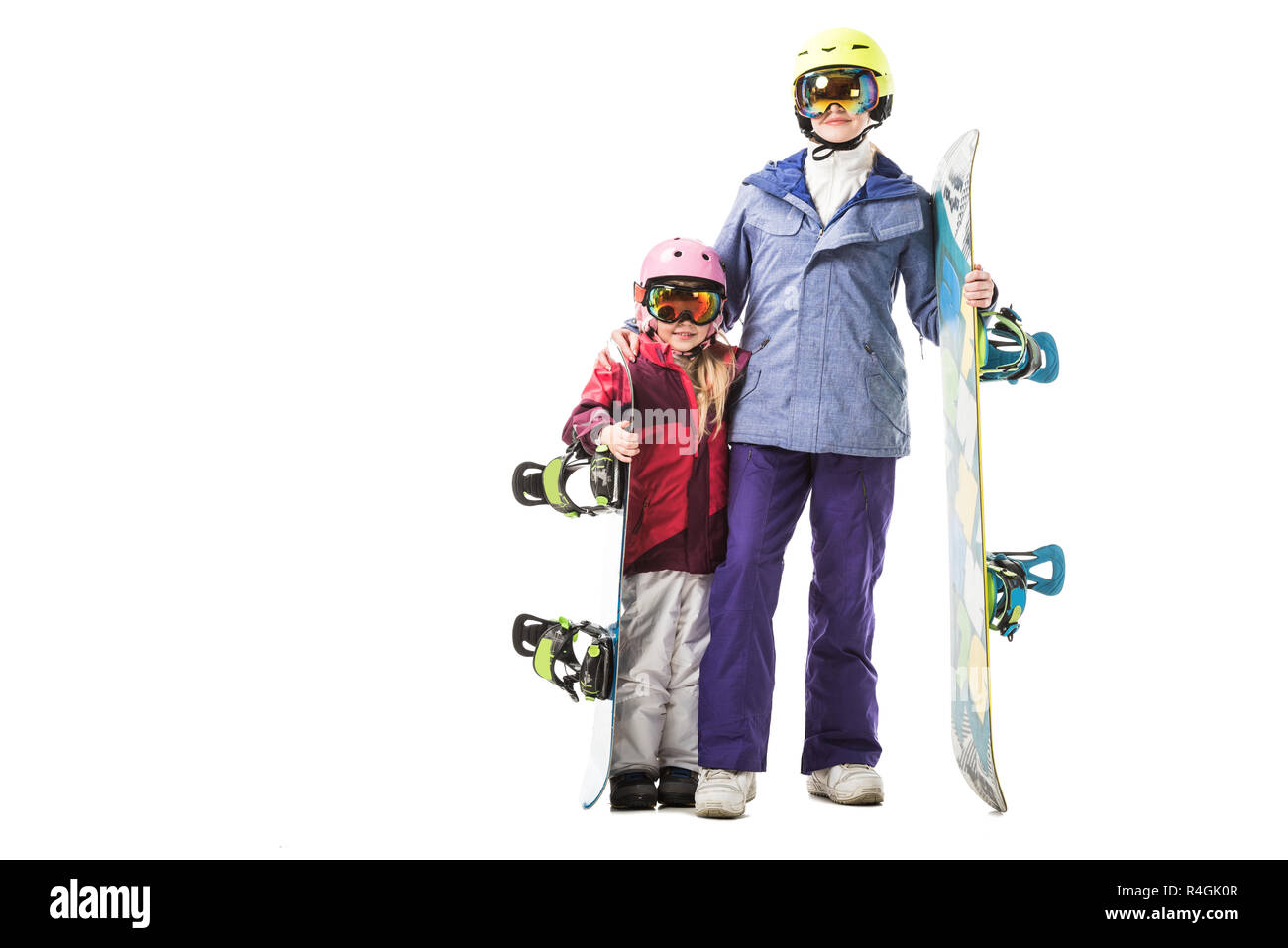 Mama und Vorschüler Tochter in Skianzuege, Schutzbrillen und Helme mit Snowboards lächelnd isoliert auf weißem Stockfoto