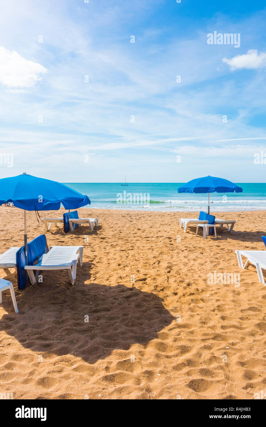 Blaue Sonnenschirme und Liegestühle am einsamen Strand, Albufeira, Algarve, Portugal Stockfoto