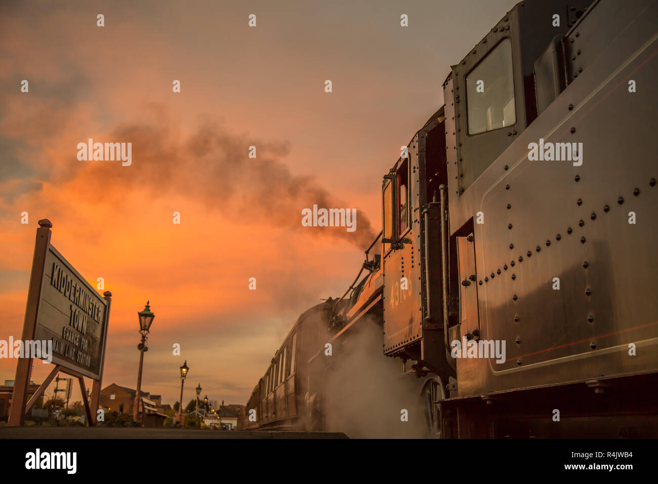 Niedriger Winkel, Seitenansicht Nahaufnahme des alten britischen Dampfzugs am Bahnsteig in leerem historischen Bahnhof am Ende des Tages mit glühendem Sonnenuntergang Abendhimmel. Stockfoto