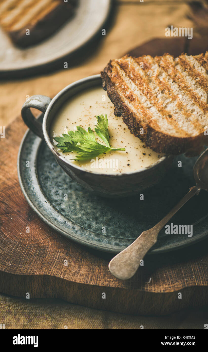 Herbst, Winter home Abendessen. Herbst Erwärmung Sellerie creme Suppe in Schale und Toast über gelb Bettwäsche Tischdecke, close-up. Komfort Essen, vegan, Vegetarisch, h Stockfoto