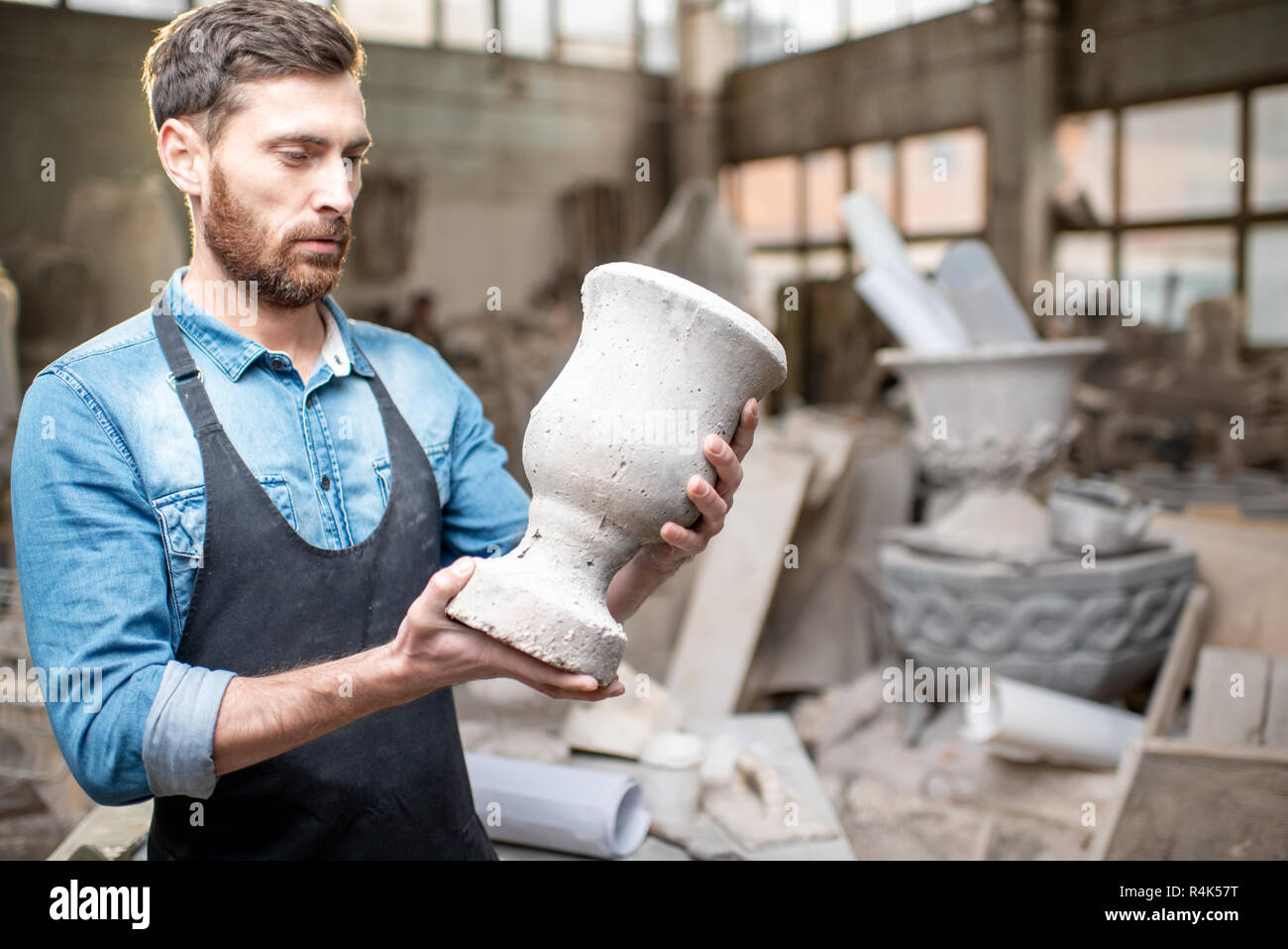 Porträt einer stattlichen Bildhauer in blauen T-Shirt und Schürze Holding alte Vase im Studio Stockfoto