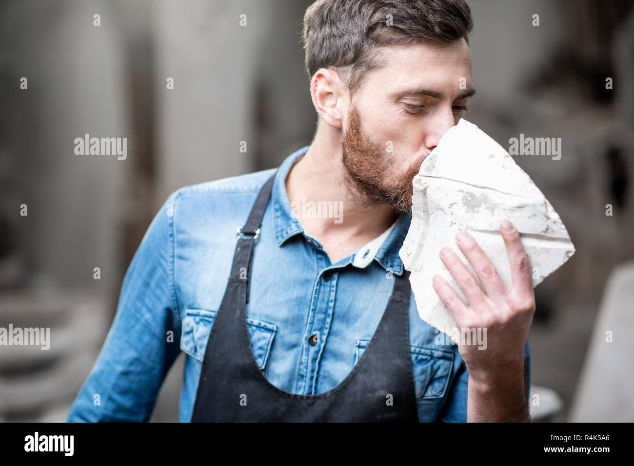 Porträt einer stattlichen Bildhauer in blauen T-Shirt und Schürze mit einem Stein im Studio Stockfoto