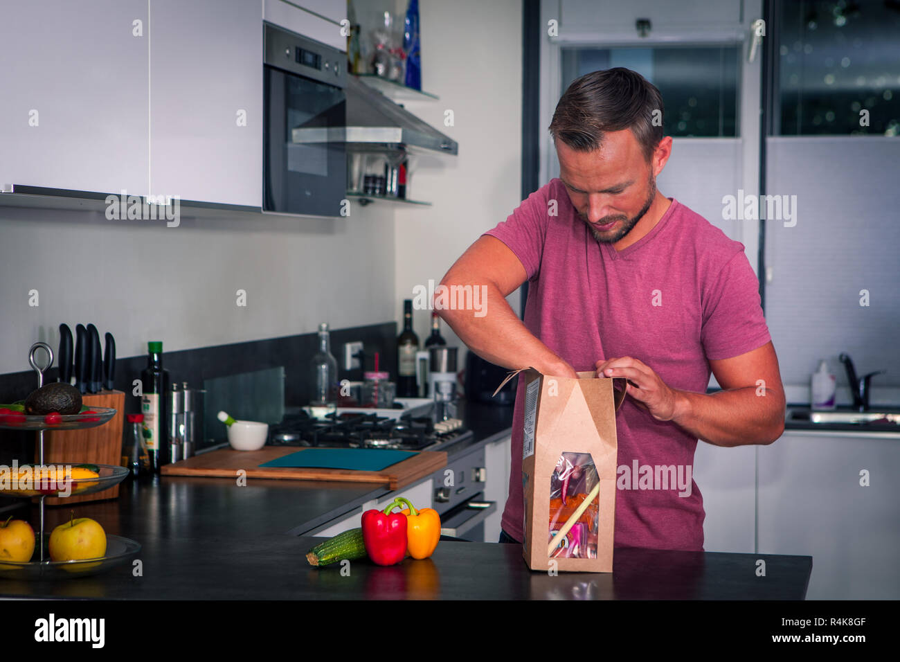 Junger Mann öffnet sich ein Paket von frischen Zutaten ein gesundes Abendessen zu machen Stockfoto