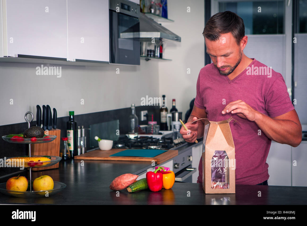 Junger Mann öffnet sich ein Paket von frischen Zutaten ein gesundes Abendessen zu machen Stockfoto