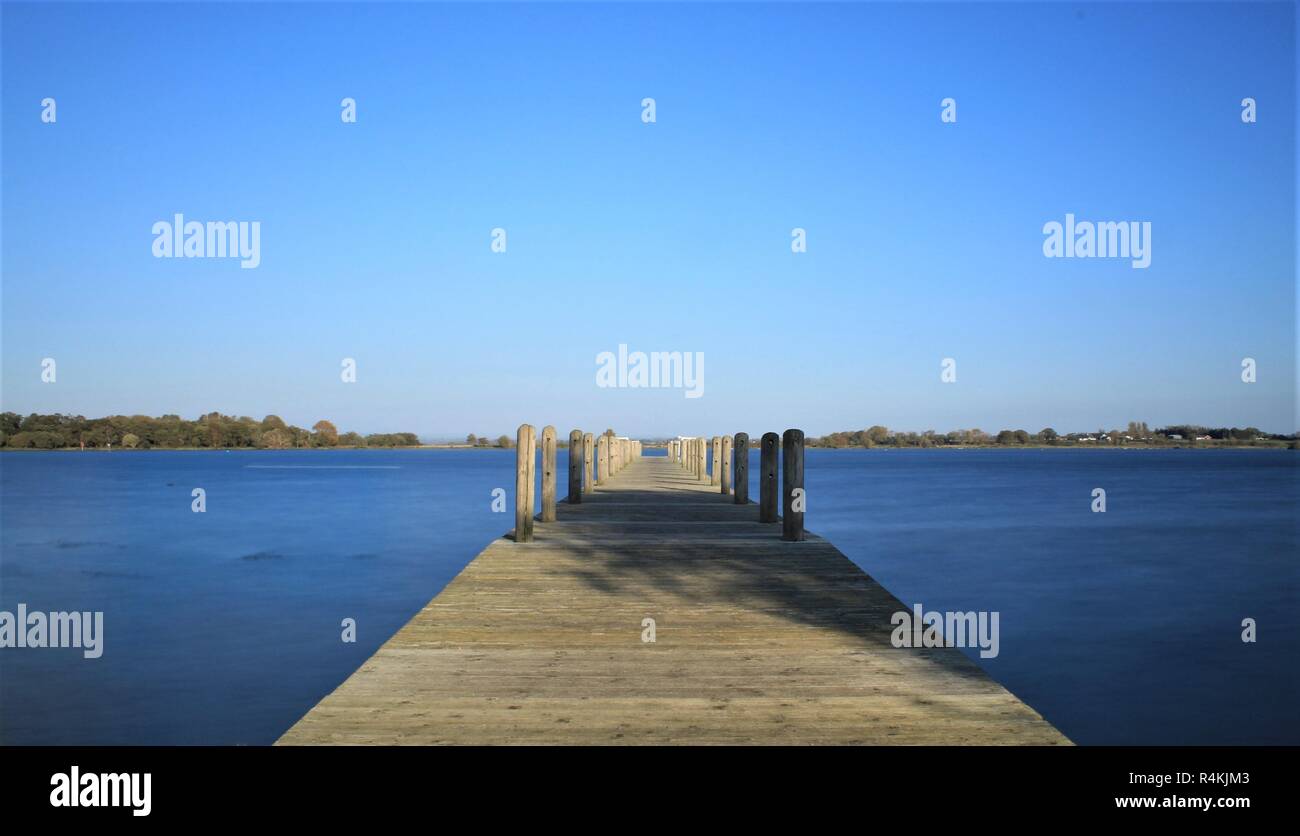 Eine leere Pier befindet sich auf ruhigen blauen Wasser unter einem wolkenlosen blauen Himmel Stockfoto