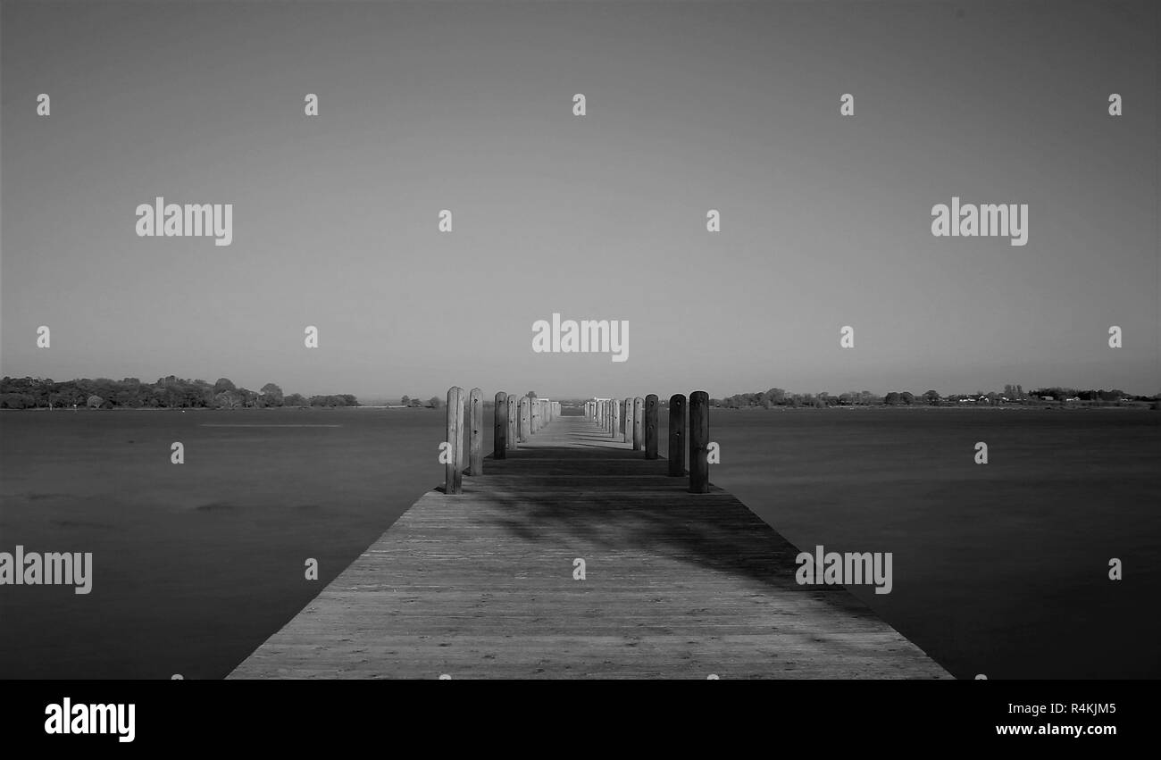 Eine leere Pier sitzt auf ruhigem Wasser unter einem wolkenlosen blauen Himmel Stockfoto