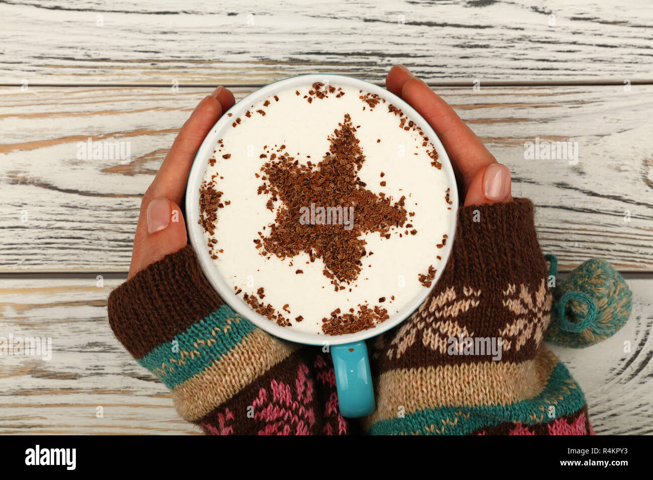 Schließen Sie zwei Frau Hände halten und Hug große volle Tasse Latte Cappuccino mit sternförmigen Schokolade auf Milchschaum über weiße Holztisch, elevat Stockfoto