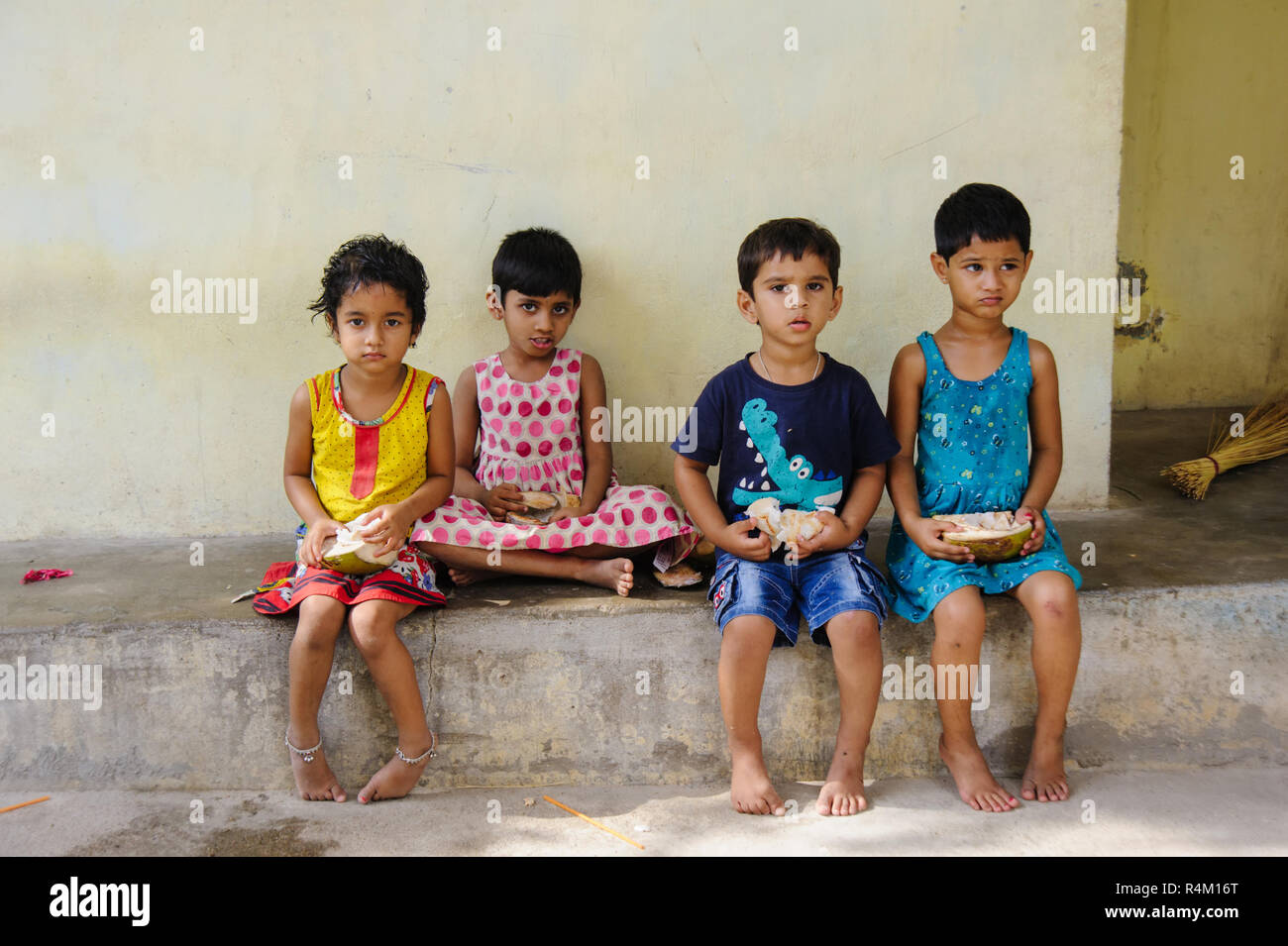 Gruppe indischer Kinder sitzt an der Straße und essen Kokosnüsse. 11. Februar 2018 Puttaparthi, Indien Stockfoto