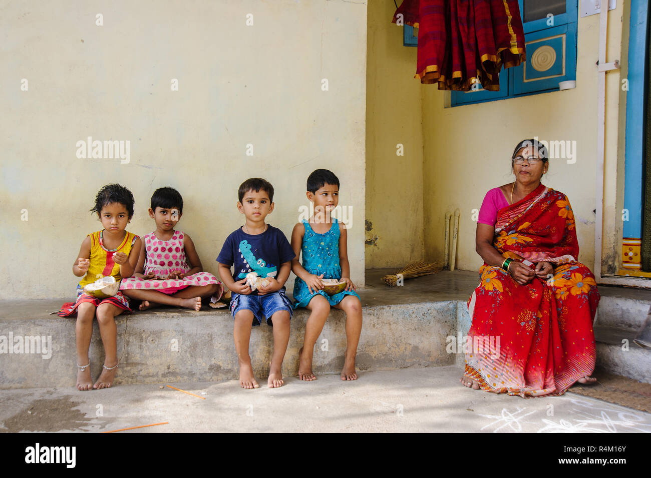 Gruppe indischer Kinder sitzt an der Straße und essen Kokosnüsse. 11. Februar 2018 Puttaparthi, Indien Stockfoto