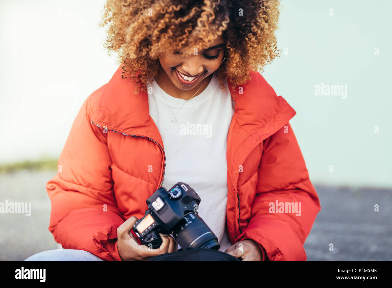 Lächelnd Afro-amerikanische Frauen sitzen im Freien mit einer DSLR-Kamera. Weibliche Touristen im Urlaub sitzt auf der Straße, die eine digitale Kamera. Stockfoto