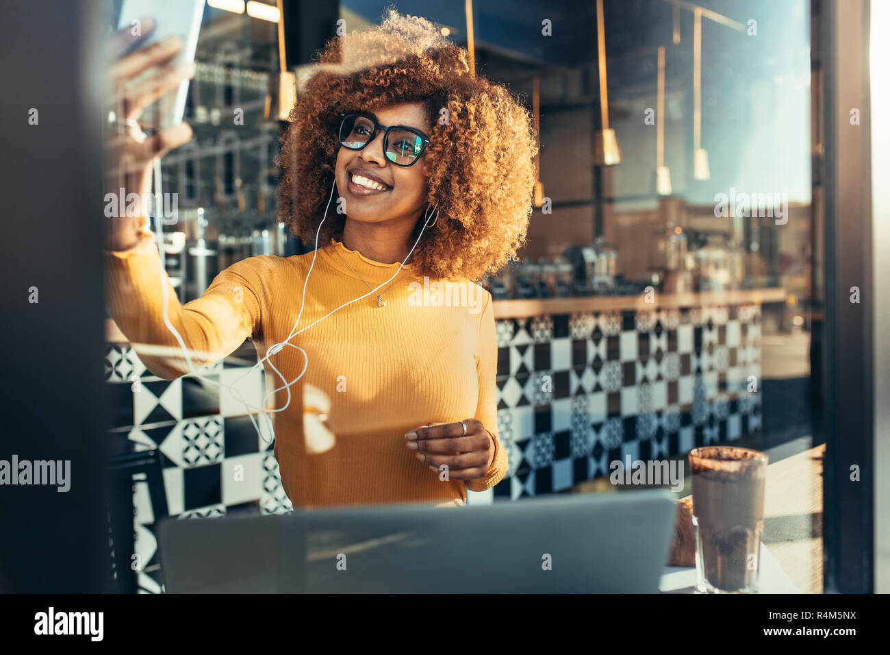 Lächelnd afro-amerikanische Frau Schoß selfie über Handy in einem Restaurant. Frau in Brillen sitzen in einem Café mit Blick auf ihre Zelle pho Stockfoto