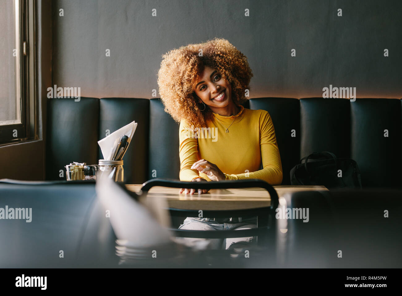 Lächelnd afro-amerikanische Frau an einem Tisch im Restaurant sitzen warten auf jemanden. Fröhliche Geschäftsfrau in einem Restaurant mit ihrer Tasche durch ihre sid Sitzen Stockfoto