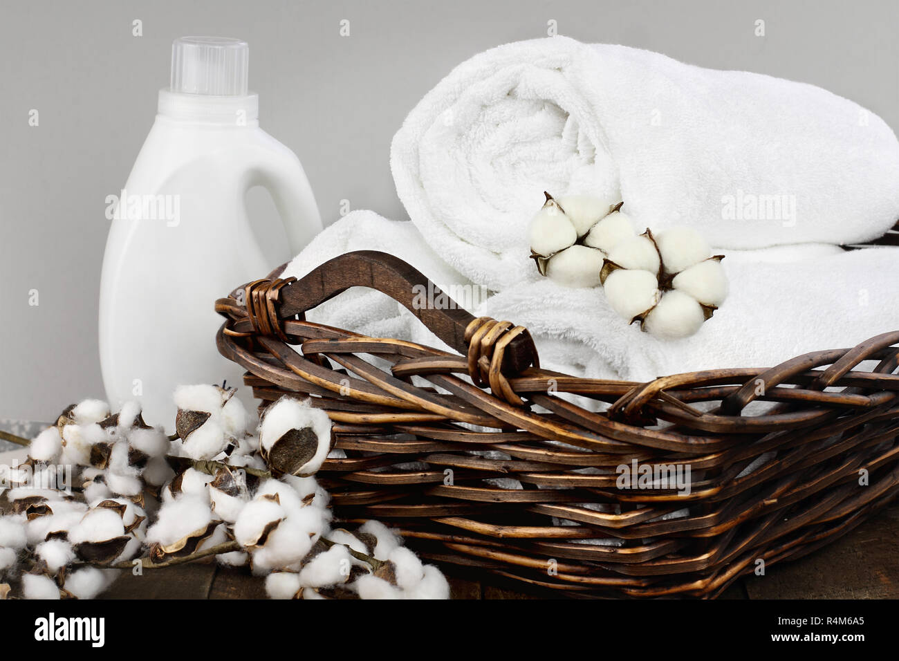 Wäsche Korb weiße flauschige Handtücher, Baumwolle, Blumen und eine Flasche flüssige Seife gegen einen unscharfen Hintergrund grau. Stockfoto