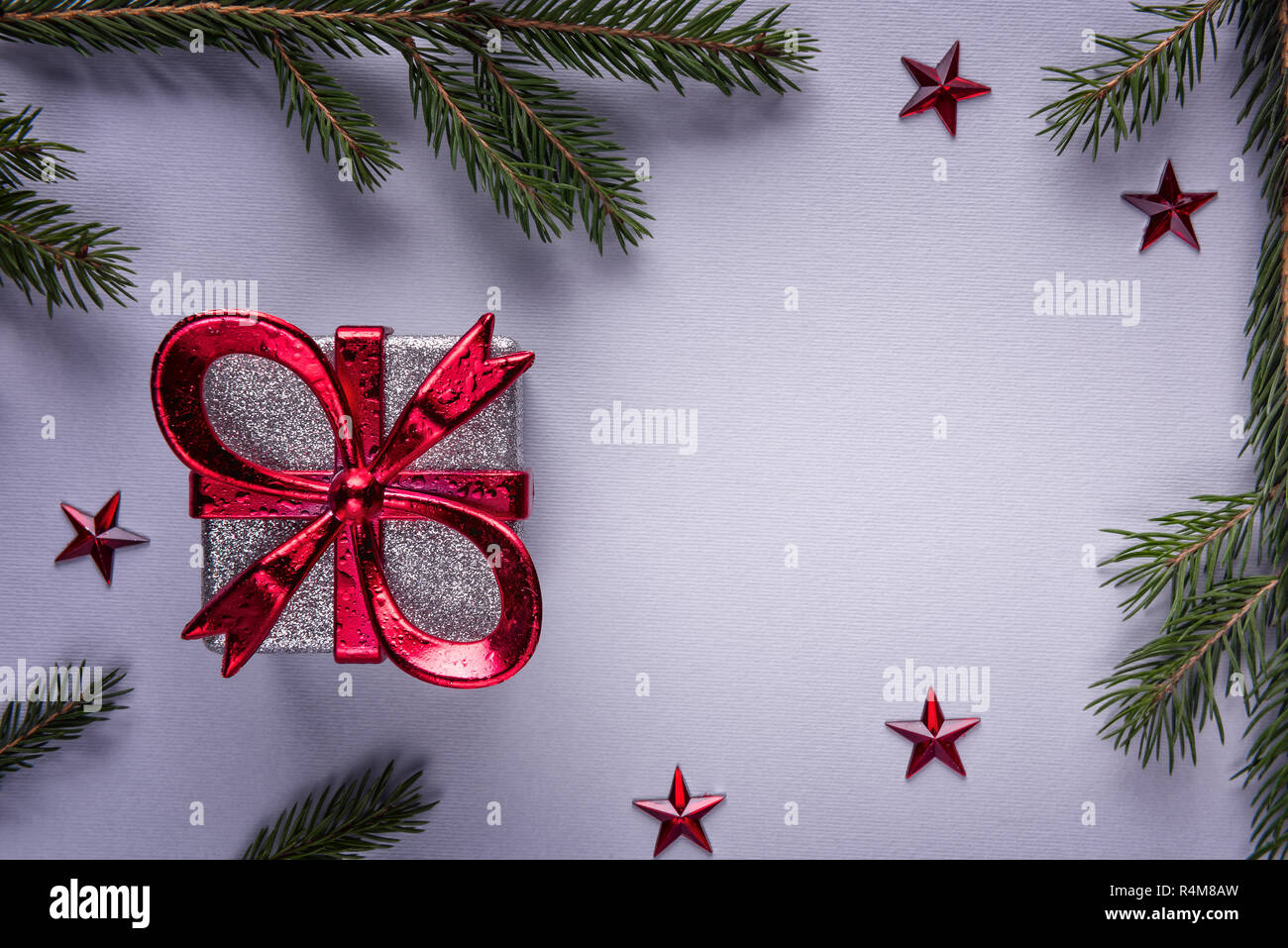 Weihnachten Grußkarte Hintergrund mit quadratischen silbernen Geschenkbox mit roter Schleife auf grauem Papier von natürlichen, grünen Tannenzweigen und roten umgeben Stockfoto