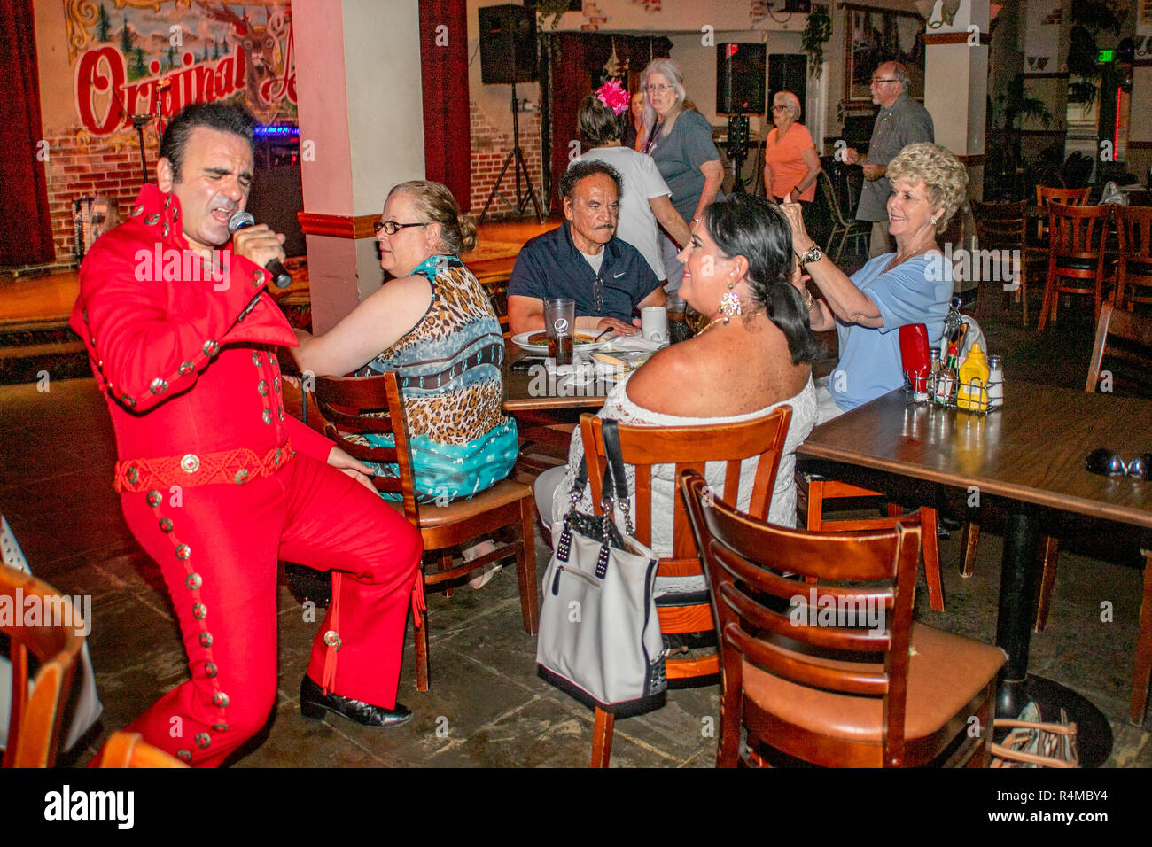 Das Tragen einer roten Overall, einer mittleren östlichen Amerikanischen Elvis Presley Imitator unterhält Erwachsene und Senioren bei einer Santa Ana, CA, Pub. Stockfoto