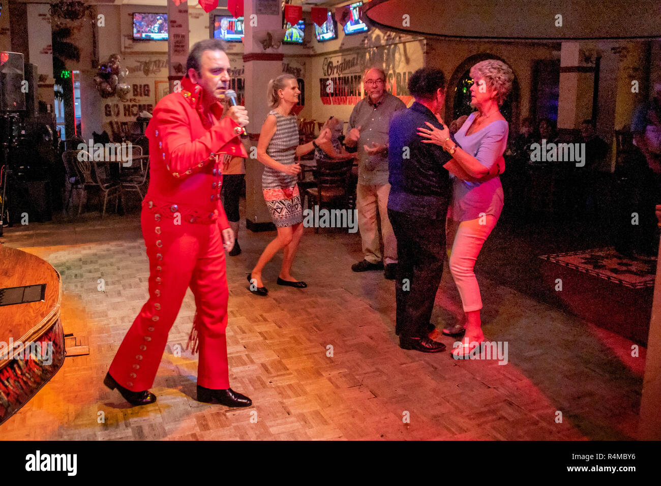 Das Tragen einer roten Overall, einer mittleren östlichen Amerikanischen Elvis Presley Imitator unterhält Erwachsene und Senioren bei einer Santa Ana, CA, Pub. Stockfoto