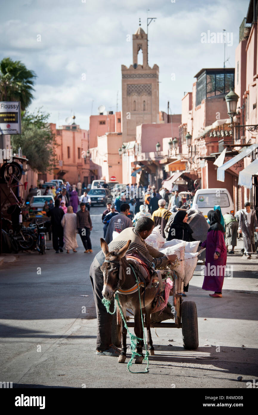 18-04-11. Marrakesch, Marokko. Fußgänger, Autos und Eseln teilen sich die Straße in der Medina, mit einem Minarett einer Moschee im Hintergrund. Foto © Simon Stockfoto