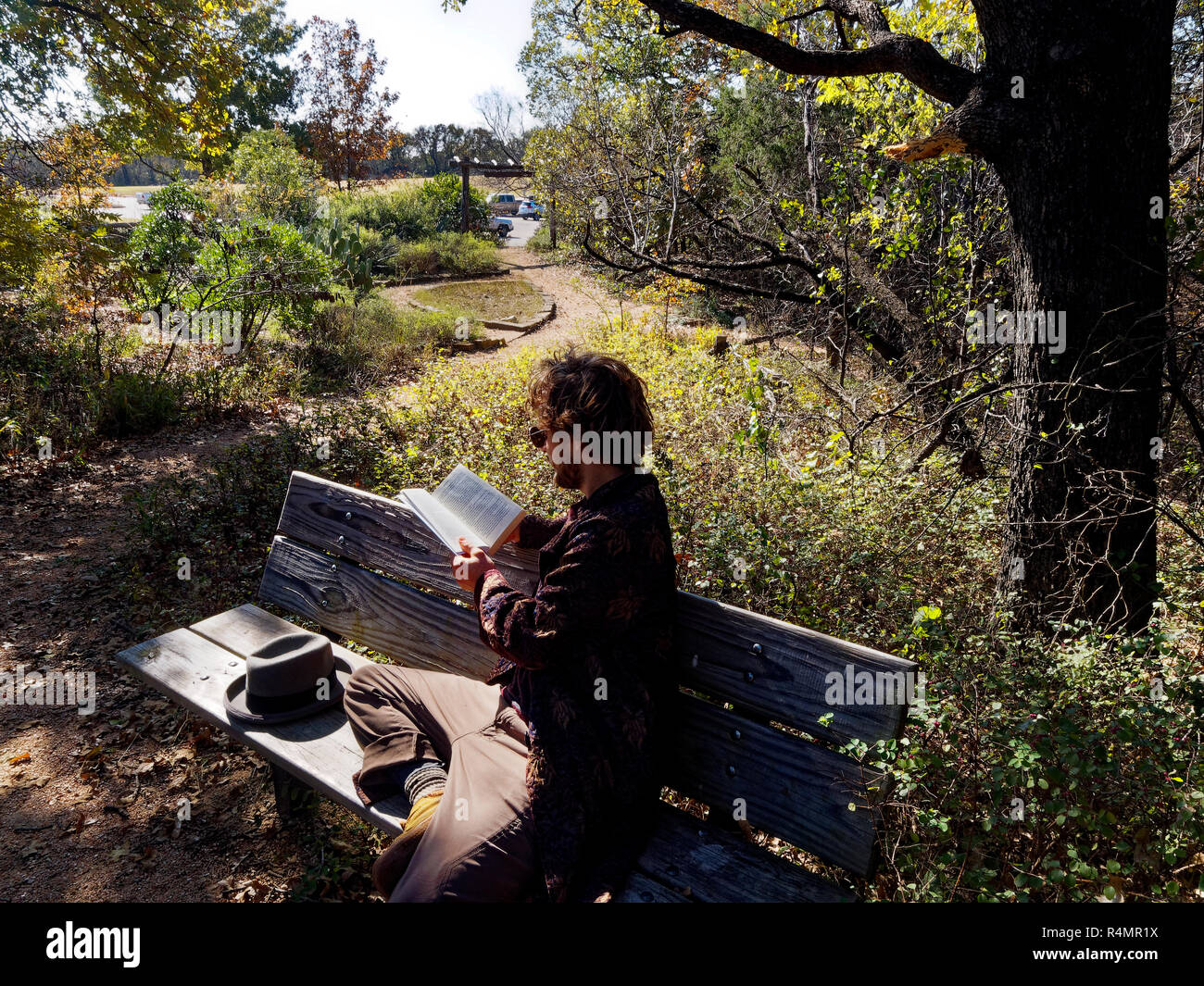 Milinial Mann erhält außerhalb in einem Park mit einheimischen Pflanzen zu lesen, noch nicht von der Hektik des urbanen Lebens umgeben. Stockfoto
