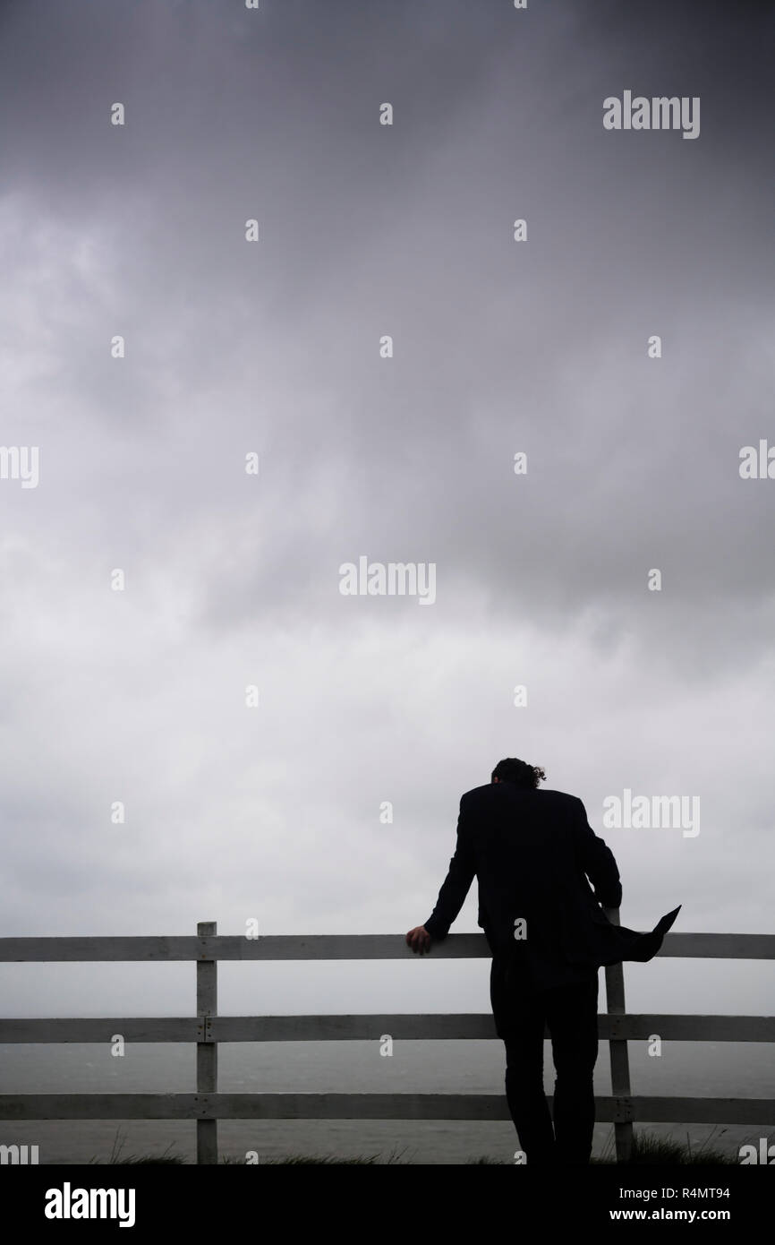Ein Mann Mit Einer Dunklen Schwarzen Mantel Allein Stehend Von Hinten Stutzte Sich Auf Einen Zaun Mit Blick Auf Das Meer Auf Einem Dunklen Brutende Bewolkt Windigen Tag Stockfotografie Alamy