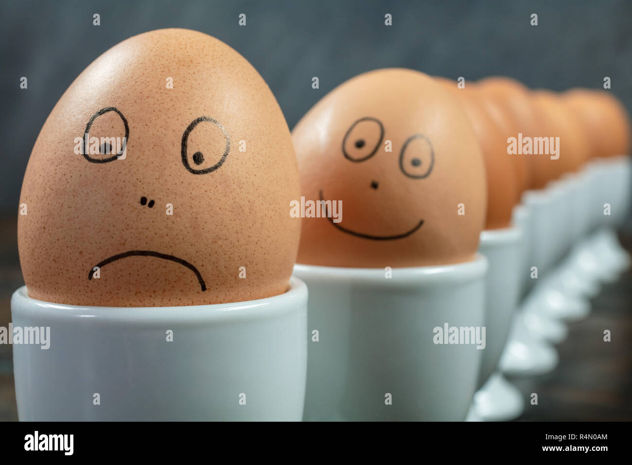 Emotionen Konzept Warteschlange oder bis von 10 gekochte Eier in Weiß  Eierbecher mit gezogenen glückliche und traurige Gesichter auf einem  Holztisch Stockfotografie - Alamy