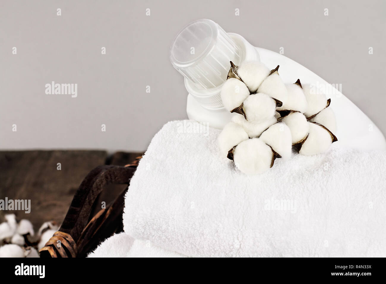 Wäsche Korb weiße flauschige Handtücher, Baumwolle, Blumen und eine Flasche flüssige Seife gegen einen unscharfen Hintergrund grau. Stockfoto