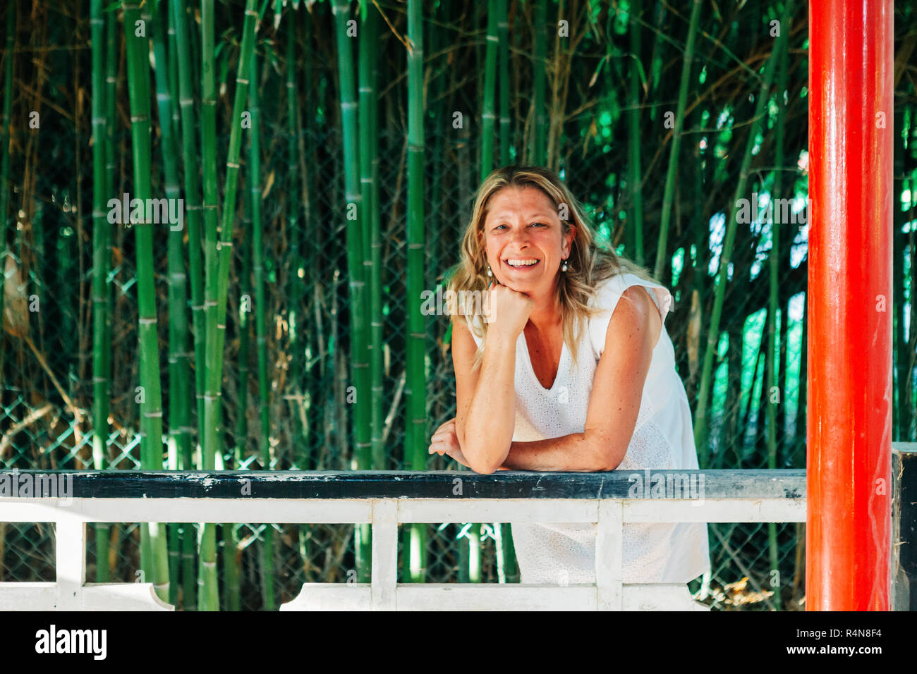 Lächelnde Frau lehnte sich auf Zaun durch Bambus Stockfoto