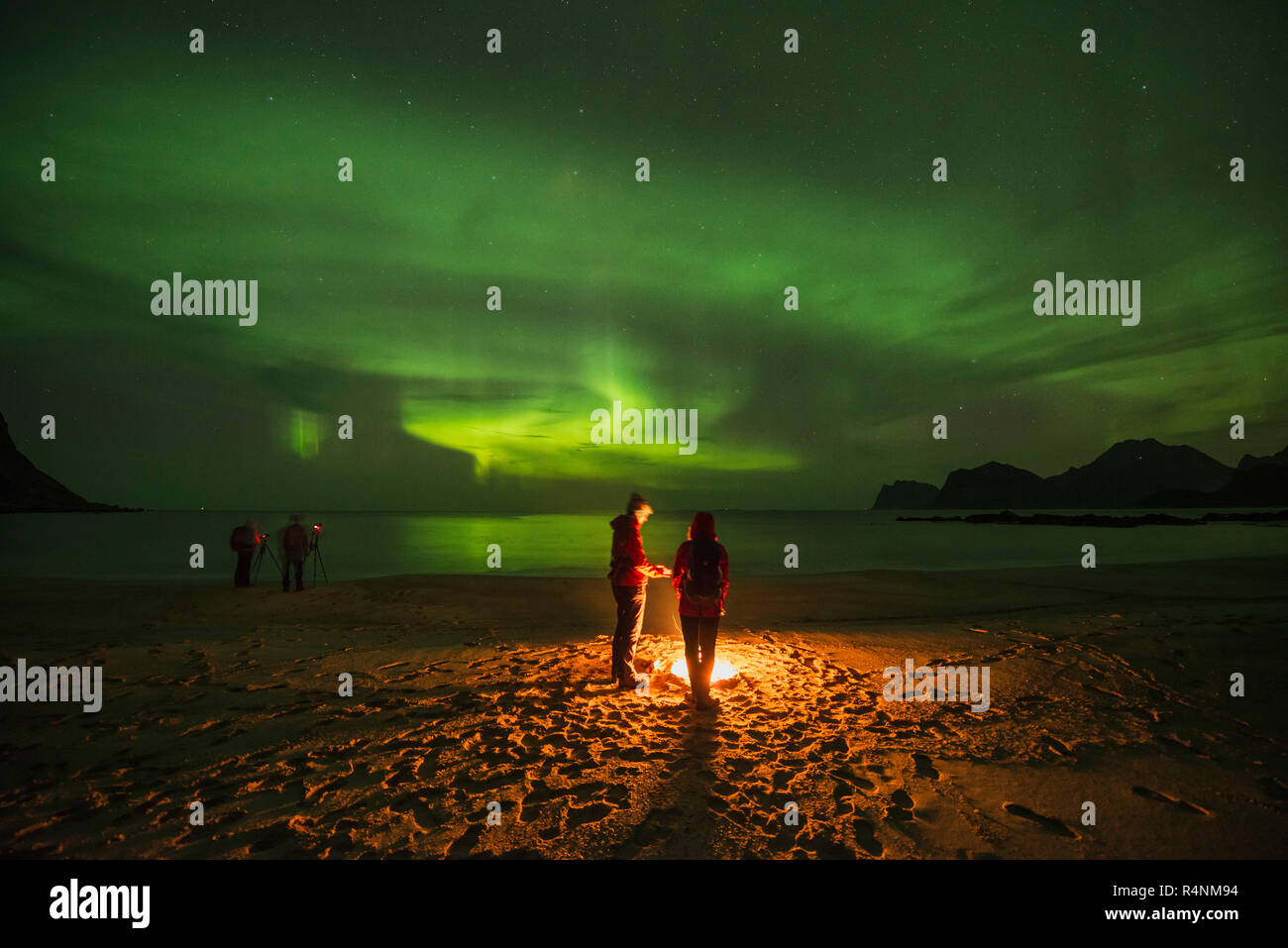 Ruhige Szene mit Menschen um Lagerfeuer am Strand unter auroraÂ borealisÂ bei Nacht, Flakstadoya, Lofoten, Norwegen Stockfoto