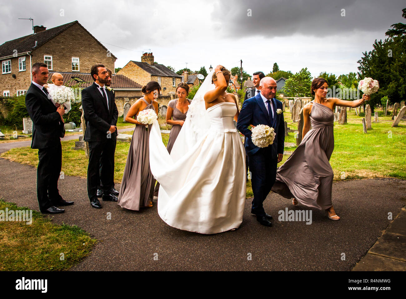 Braut mit Unternehmen, zur Kirche zu gehen für Ihre Hochzeit an einem windigen Tag Stockfoto