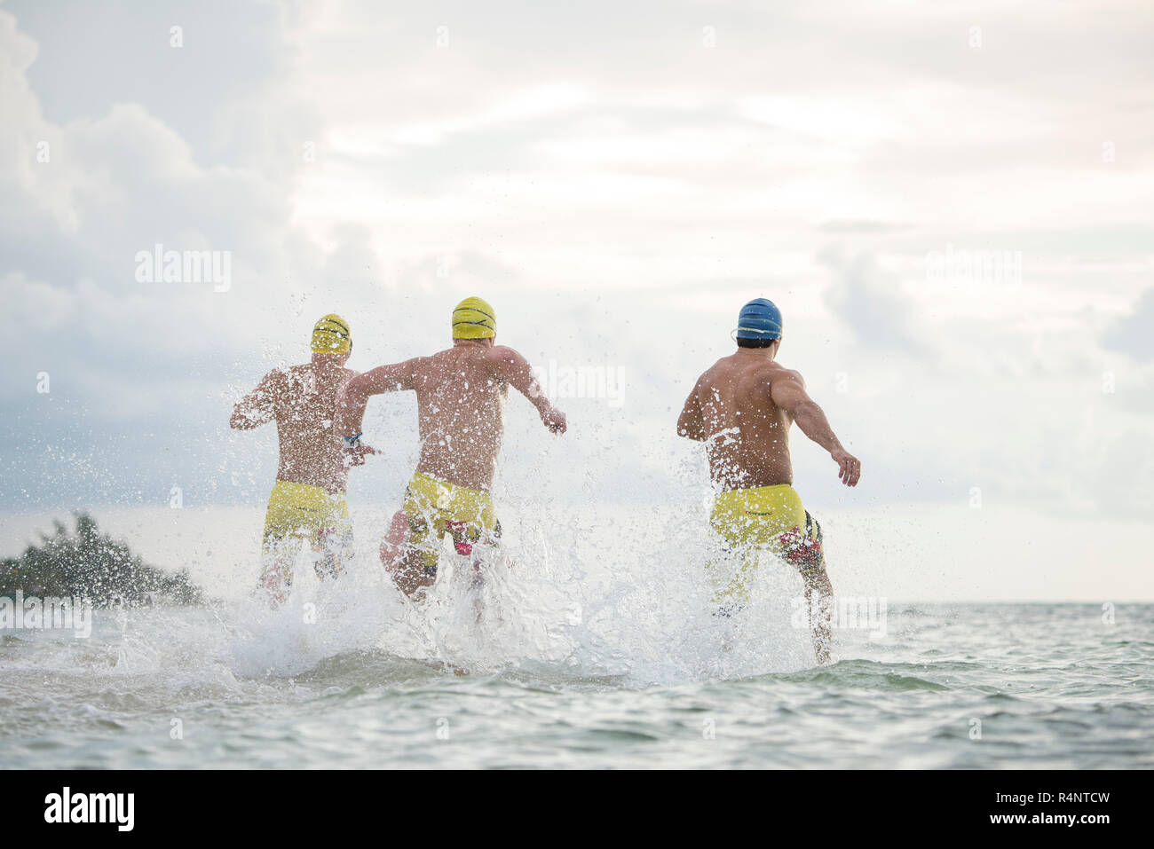 Ansicht der Rückseite drei Männer in Badekappen und Badehose in Meer in Playa del Carmen, Quintana Roo, Mexiko läuft Stockfoto