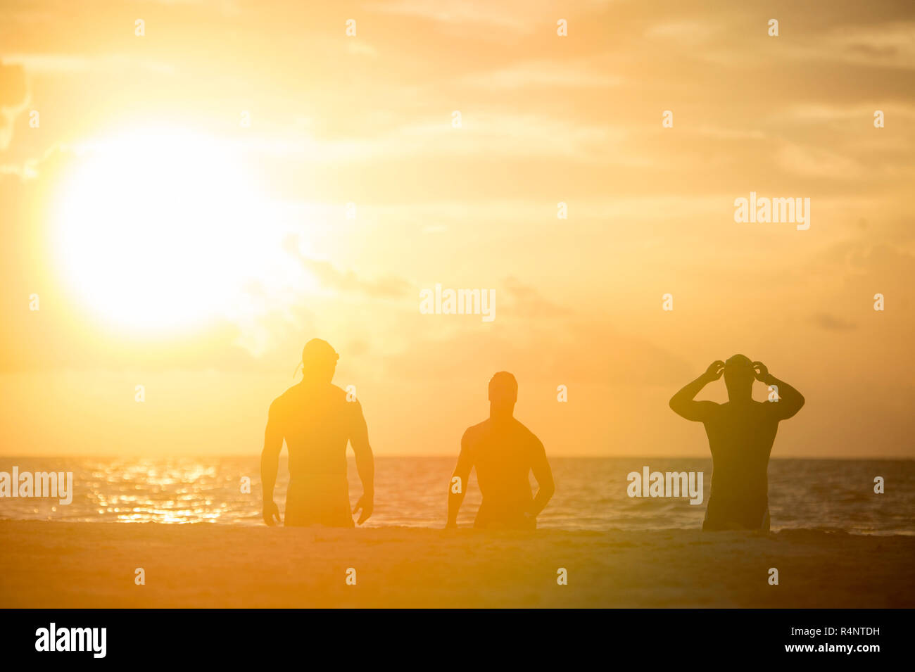 Blick auf die Silhouetten der drei Männer in badekappen am Strand bei Sonnenaufgang, PlayaÂ QuintanaÂ delÂ Carmen, Roo, Mexiko Stockfoto