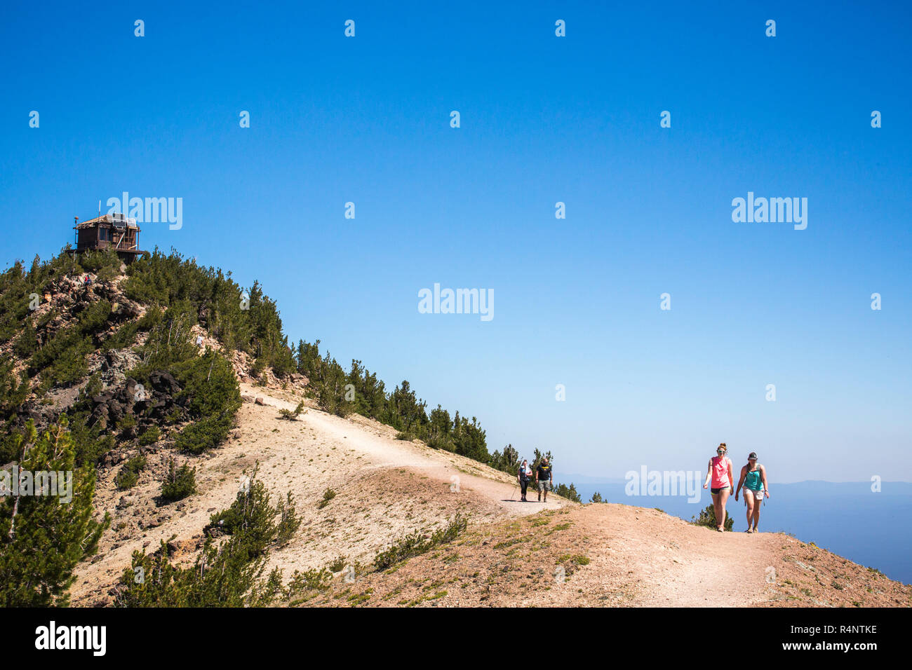 Zwei Wanderer stehen auf einem Ridge Wanderweg führt zu einem Gipfel mit Aussichtsturm auf einem sonnigen Tag, Crater Lake, Oregon, USA Stockfoto